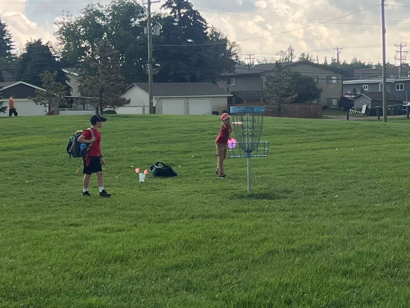 Two kids on a grassy field putting a disc into a portable disc golf basket at an Alberta Youth Disc Golf session.